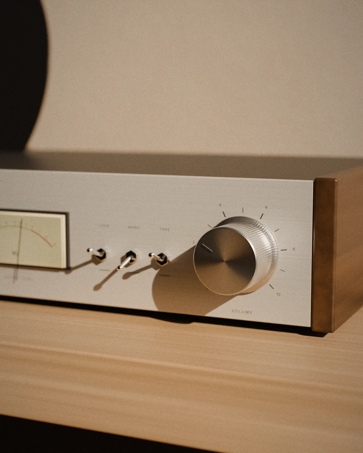 Close-up of a silver amplifier front panel in warm light: a knurled volume knob, three toggle switches and a softly lit level meter.